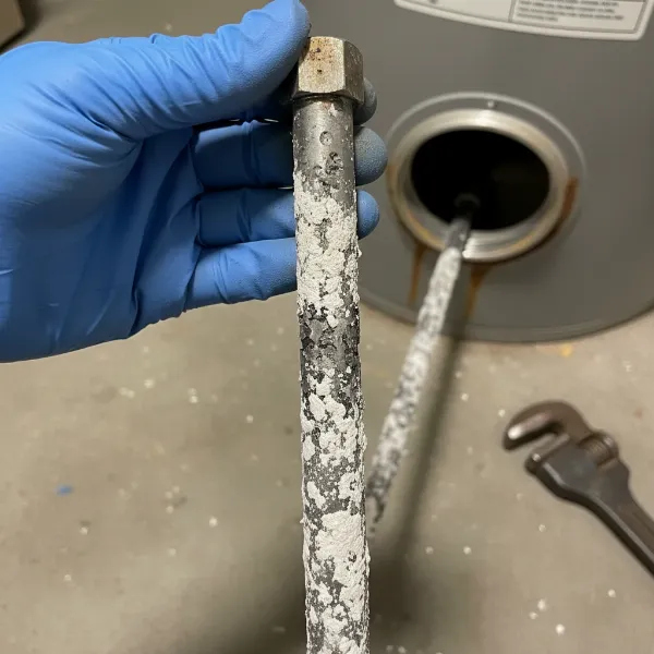 A close-up view of a hand inspecting a partially removed anode rod from a water heater for wear.